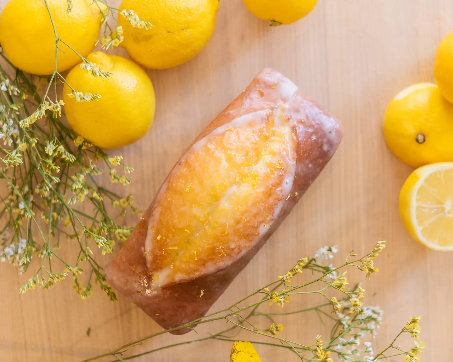 Cake au citron glacé posé sur bois clair entouré de citrons